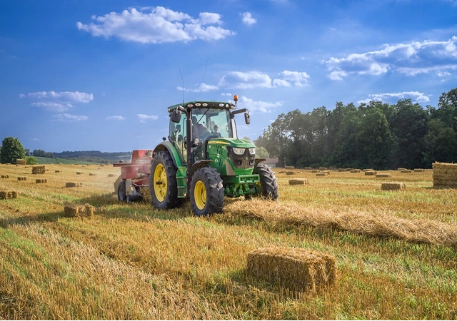 Trator agrícola operando em campo com fardos de palha.