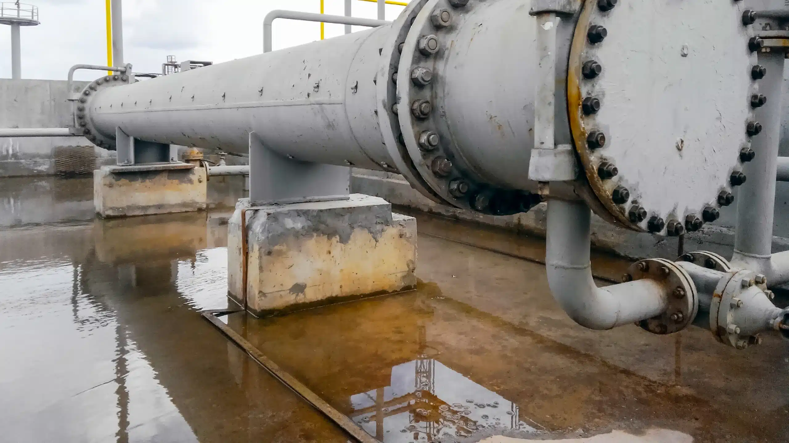 Piso de concreto sem revestimento em bacia de contenção, com líquido acumulado e manchas de desgaste nos blocos de apoio.